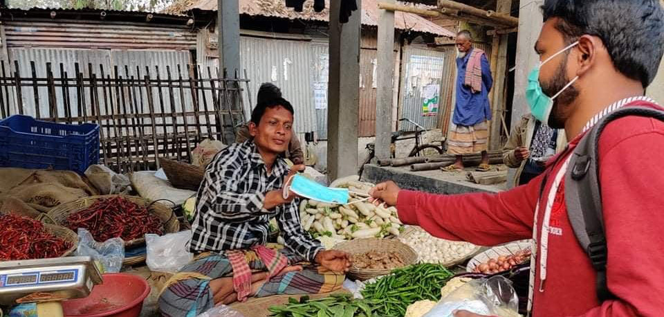 Photo of a person distributing a surgical face mask to another person during the COVID-19 pandemic in Bangladesh